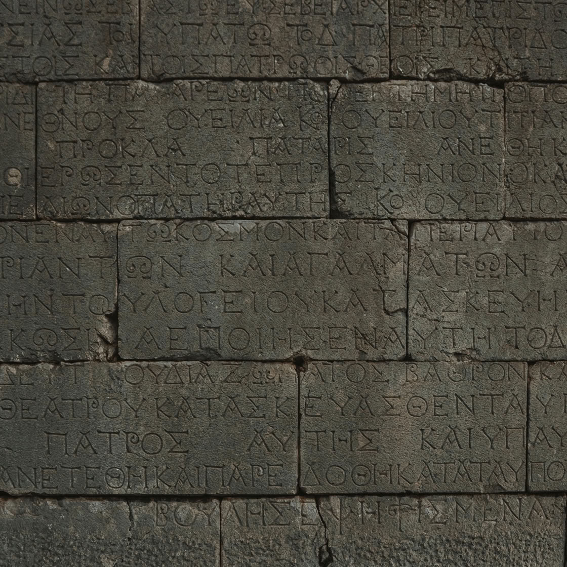 Close-up of an ancient stone wall with Greek inscriptions engraved on it.