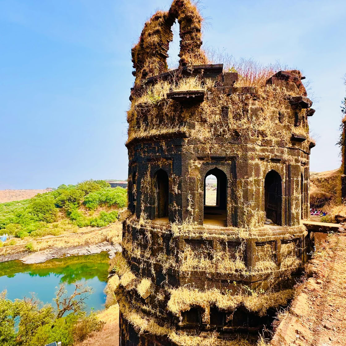 Detailed view of a weathered fort tower in ruins, set against a vibrant blue sky and lush greenery.