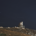 Long exposure of star trails above an ancient hillside tower under restoration at night.