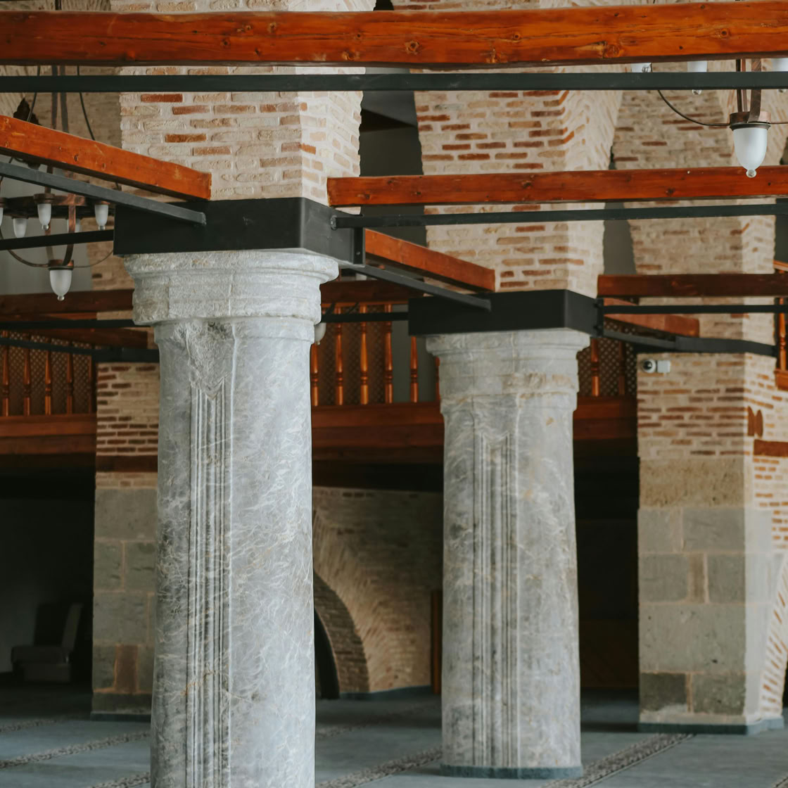 Interior view showcasing historic brick and stone columns with wooden beams inside an ancient building.